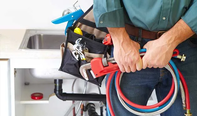 Sam T's plumber with tool belt and water supply lines under a kitchen sink